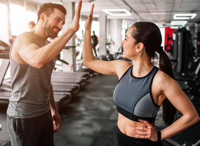 A beautiful girl and her well-built boyfriend are greeting each other with a high-five. They are happy to see each othr in the gym. Young people are ready to start their workout.
