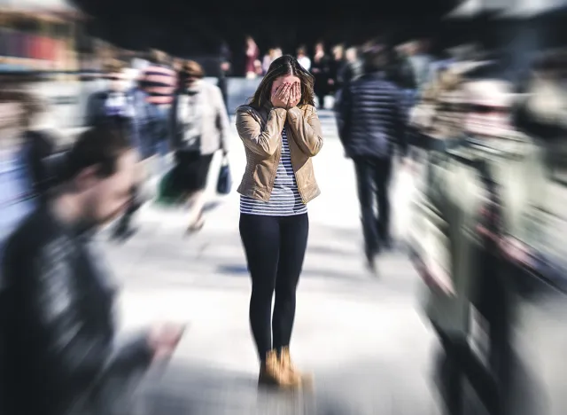 Panic attack in public place. Woman having panic disorder in city. Psychology, solitude, fear or mental health problems concept. Depressed sad person surrounded by people walking in busy street.