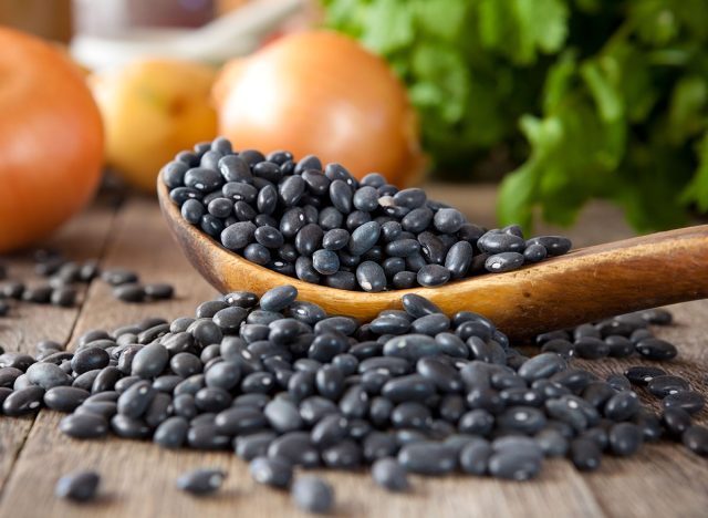 Black beans in a wooden spoon with cilantro and onions in the background