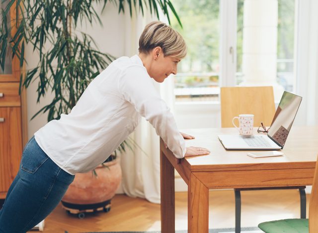 Fit businesswoman doing stretching exercises on a wooden office table while working on her laptop computer