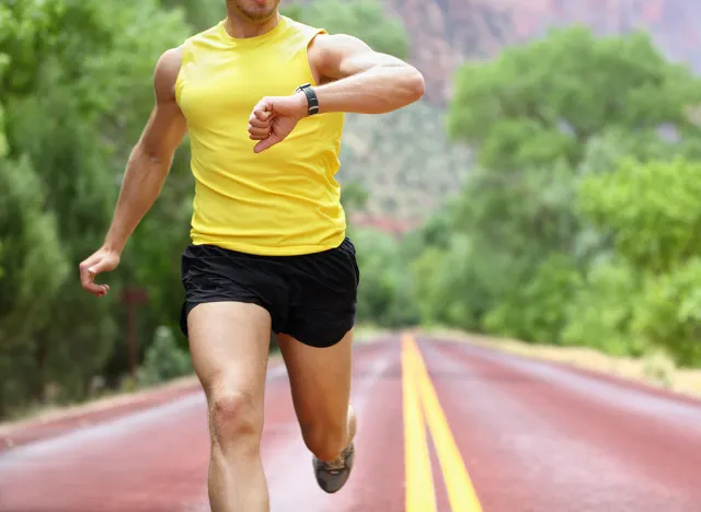 Runner with heart rate monitor sports smart watch. Man running looking at his pulse outside in nature on road with smartwatch.