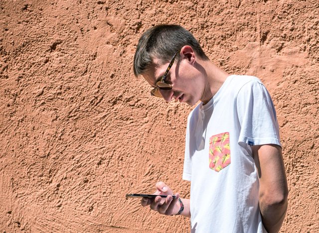 Cividale, Italy - June 3, 2018: caucasian young man using a smartphone with a posture that can cause tech or text neck syndrome