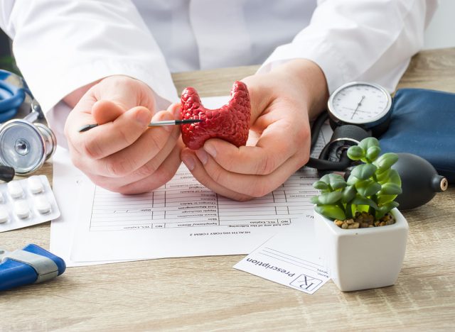 At doctors appointment physician shows to patient shape of thyroid gland with focus on hand with organ. Scene explaining patient causes and localization of diseases of thyroid and endocrine system