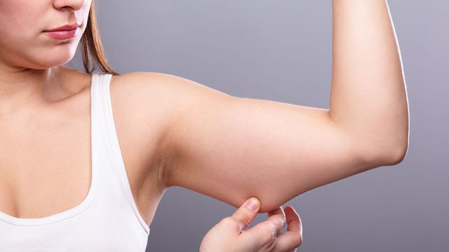 Close-up Of A Woman Holding Arm With Excess Fat On Grey Background