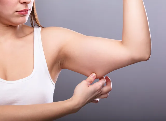 Close-up Of A Woman Holding Arm With Excess Fat On Grey Background