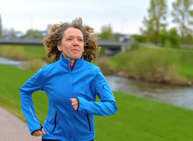 Fit athletic middle-aged woman jogging on a road alongside a canal approaching the camera with a smile of pleasure in a healthy lifestyle concept