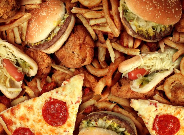 Fast food concept with greasy fried restaurant take out as onion rings burger and hot dogs with fried chicken french fries and pizza as a symbol of diet temptation resulting in unhealthy nutrition.