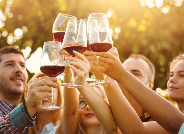 Group of friends in a wine tasting tour at vineyard - Hands toasting red wine glasses with sun flare - Friendship and travelling concept