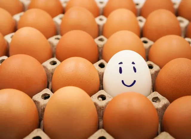 A white chicken egg among many brown eggs with happy ,relax and smiley face, represent concept of differentiation, relax ,optimistic , growth mindset , freedom and independent