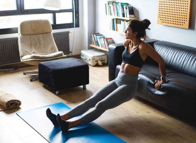 Fitness workout at home. Healthy fit young woman doing triceps dips exercise in the living room.