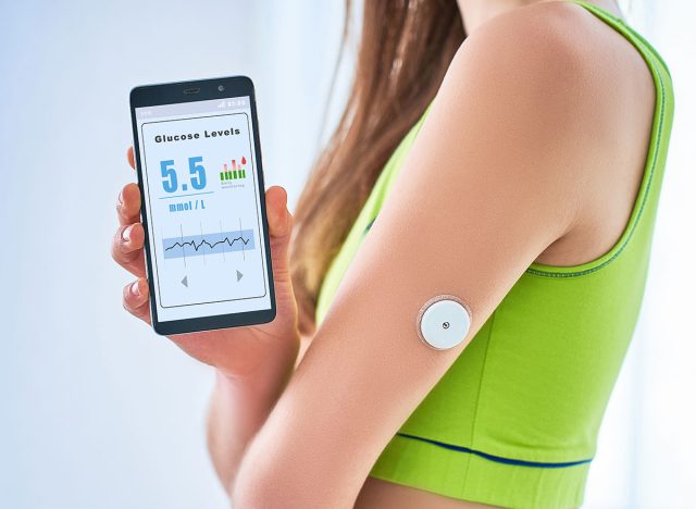 Woman diabetics control and checking glucose level with a remote sensor and mobile phone. Continuous online monitoring glucose levels without blood. Digital medical technology in diabetes treatment