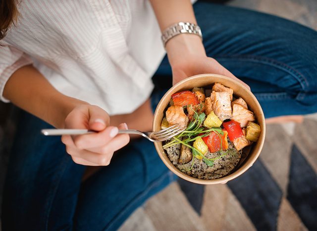 Girl holds a paper plate with healthy food sitting on the floor. Home delivery food. Healthy eating concept. When you stay at home.