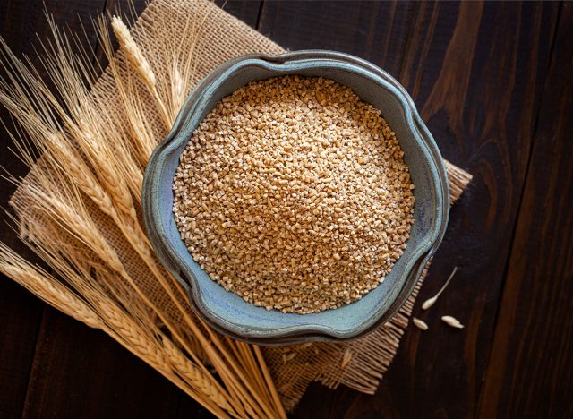 Overhead view of steel cut oats in a small bowl on a wooden surface with an accent of burlap and dried oat stems