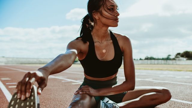 Athlete doing stretching exercises on running track. Woman runner stretching leg muscles by touching his shoes and looking away.