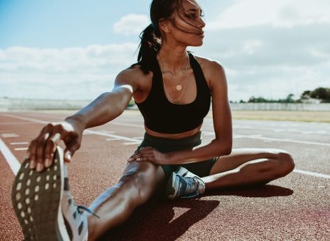 Athlete doing stretching exercises on running track. Woman runner stretching leg muscles by touching his shoes and looking away.