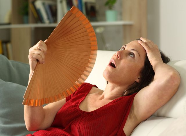 Adult woman fanning suffering heat stroke sitting in the livingroom at home