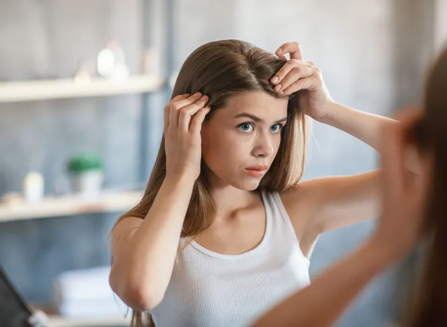 Millennial girl with hair loss problem looking in mirror at home