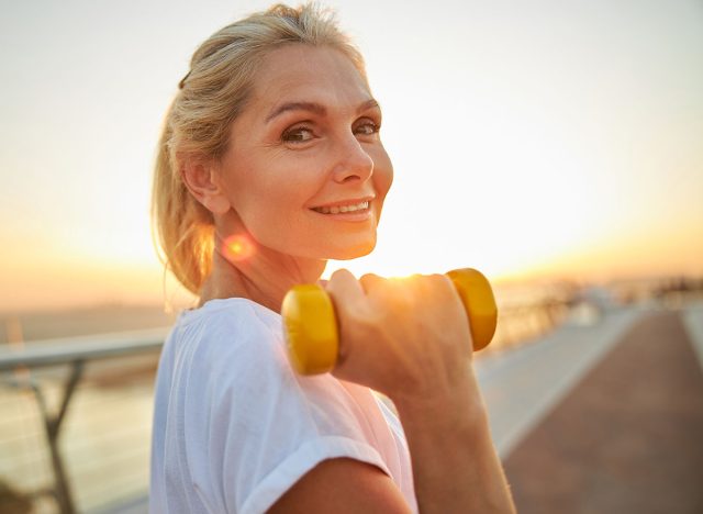 Portrait of a good-looking cheerful middle-aged athletic woman with a dumbbell posing for the camera