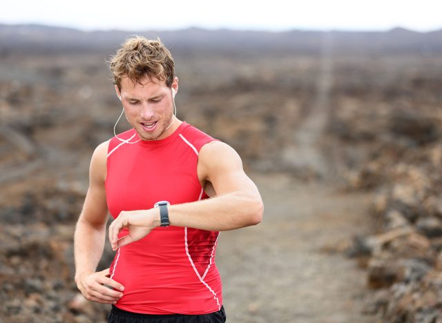 Running athlete man looking at smartwatch heart rate monitor GPS smart watch. Runner listening to music in earphones. Athlete resting tired after training on Big Island, Hawaii, USA.