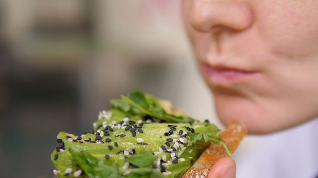 Diverse Mediterranean cuisine for health benefits. Vegan woman bites veggie rich toast with avocado slices and leafy greens