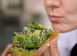 Diverse Mediterranean cuisine for health benefits. Vegan woman bites veggie rich toast with avocado slices and leafy greens