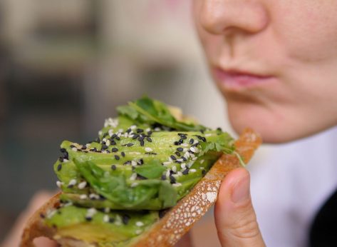 Diverse Mediterranean cuisine for health benefits. Vegan woman bites veggie rich toast with avocado slices and leafy greens