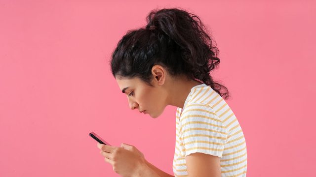 Young woman with bad posture using mobile phone on color background
