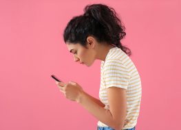 Young woman with bad posture using mobile phone on color background