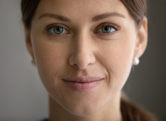 Crop close up portrait of young Caucasian green-eyed woman look at camera posing. Smiling millennial beautiful female show healthy glowing soft face skin after facial treatment. Cosmetology concept.