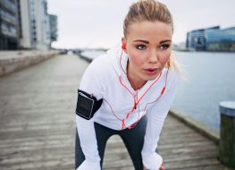 Young woman taking a break from exercise outdoors. Fit young female athlete stopping for rest while jogging along the river.