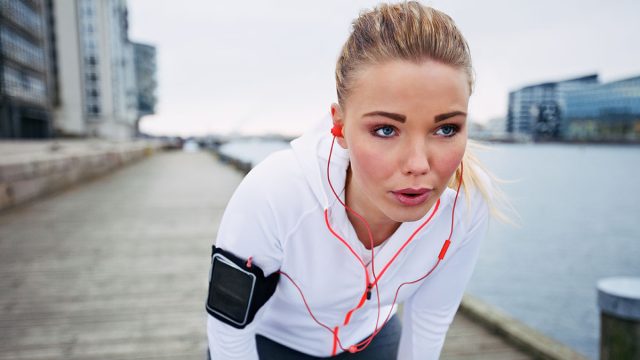 Young woman taking a break from exercise outdoors. Fit young female athlete stopping for rest while jogging along the river.