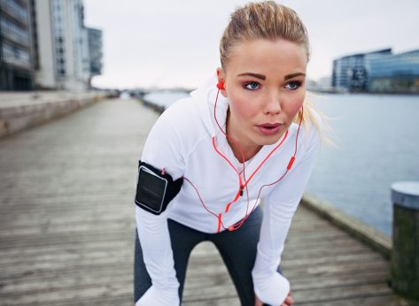 Young woman taking a break from exercise outdoors. Fit young female athlete stopping for rest while jogging along the river.