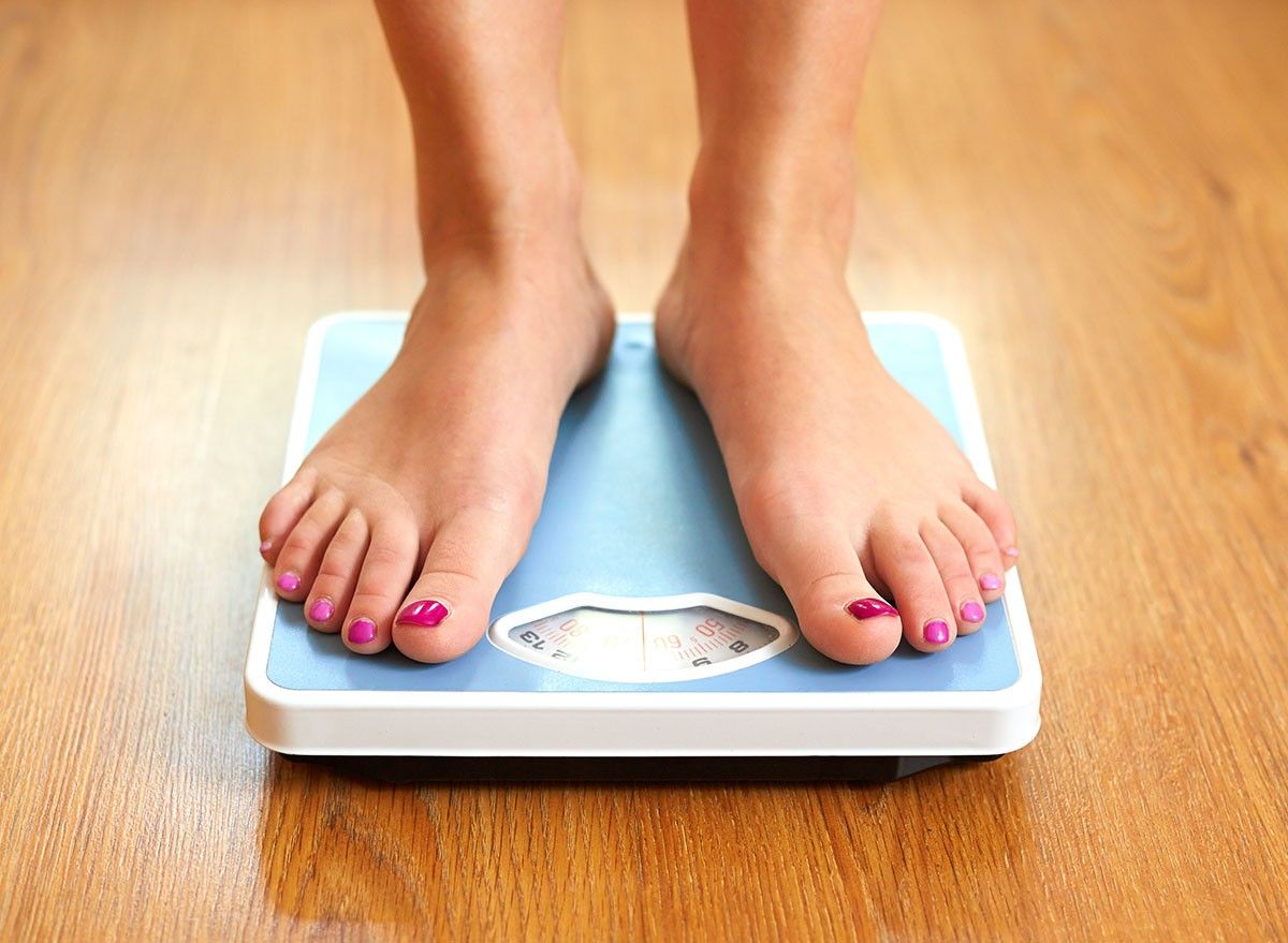 Female bare feet with weight scale on wooden floor