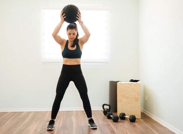 Athletic woman in her 30s with strong arms and a toned body throwing a medicine ball during her functional training at home