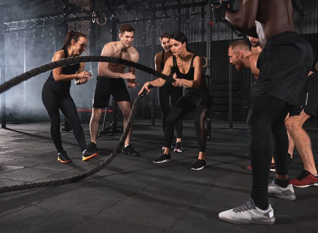 fit woman exercising with battle ropes during strength workout in cross functional gym, copy space. strong female concentrated on training