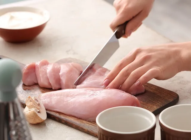 Woman cutting chicken fillet in kitchen, closeup