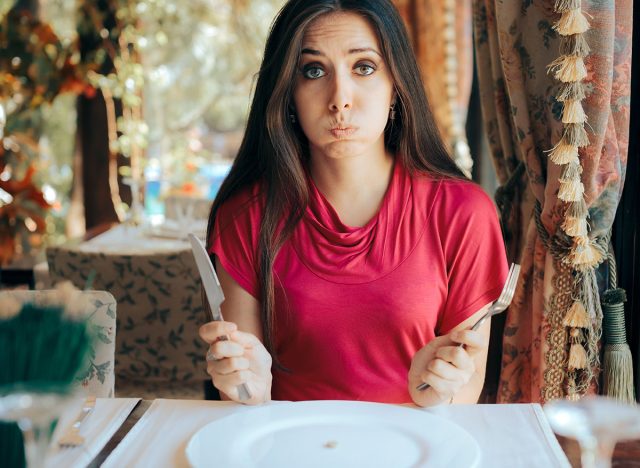Stressed Woman Having a Pill Before the Meal in a Restaurant. Unhealthy dieting with extreme measures of being in a caloric deficit