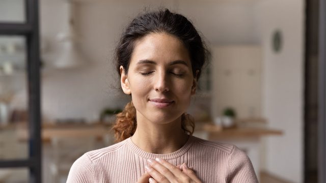 Close up of calm young Caucasian woman hold hands on heart chest feel grateful and thankful. Happy millennial female show gratitude, love and care, pray or visualize. Religion, faith concept.