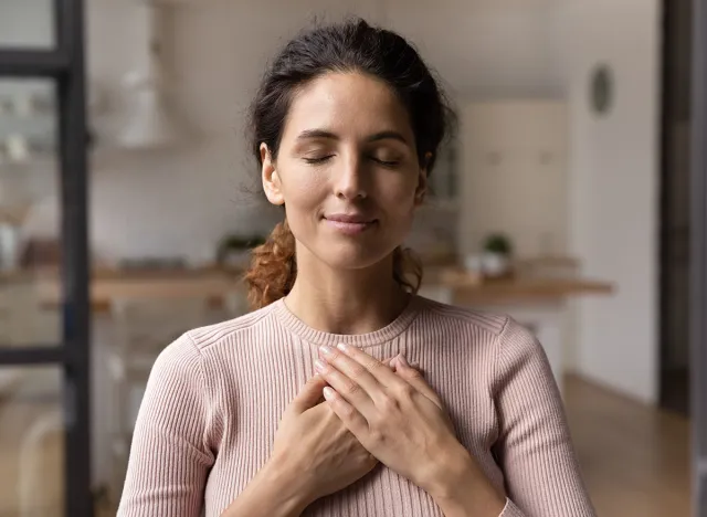 Close up of calm young Caucasian woman hold hands on heart chest feel grateful and thankful. Happy millennial female show gratitude, love and care, pray or visualize. Religion, faith concept.