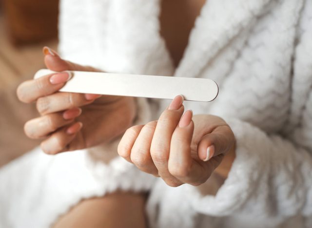 Closeup photo of young womans hand makes herself a manicure, files her nails with a nail file. Personal hygiene