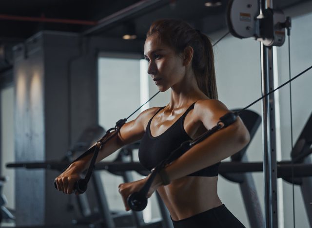 Sporty woman exercising on multistation at gym for arm and shoulders muscles. Fitness exercising in gym.