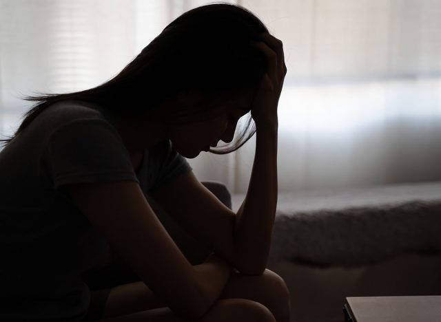 Depressed woman sitting alone on the bed with hands on head feel stress, sad and worried in the dark bedroom and low light environment