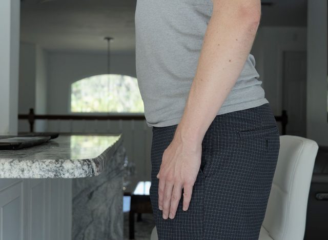 Man standing with anterior pelvic tilt posture. This man has visible tilting forward of his upper pelvis and visible lumbar lordosis.