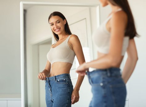 Weight Loss. Happy Lady Wearing Jeans After Slimming Comparing Size Before And After Dieting Posing Near Mirror Standing At Home. Cropped Shot, Selective Focus