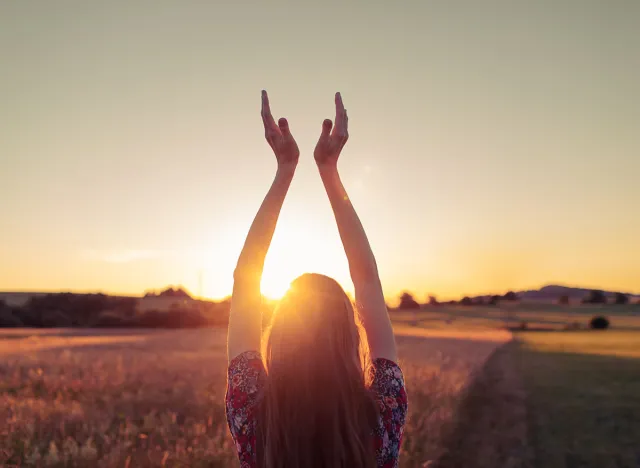 Happy woman holding hands up to the sun at dawn. Freedom and spirituality concept.