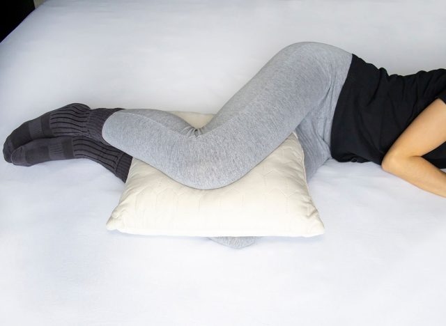 Leg cushion for sleeping for knee pain. Orthopedic pillow between the legs of a lying woman in pajamas.