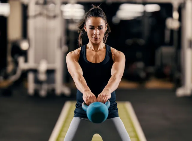 A bodybuilder in shape is swinging kettlebell while standing in a gym.