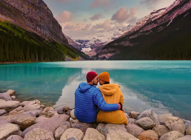 Lake Louise Banff National Park in the Canadian Rocky Mountains. A young couple of men and women sitting on a rock by the lake during a cold day in Autumn in Canada watching the sunset at the lake