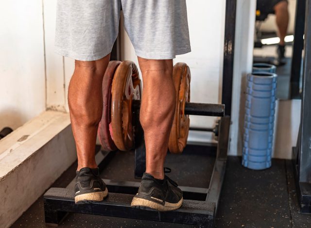 Dedicated anonymous man at the gym setting does calf raises on a weight-loaded machine with plates, focusing on lower body strength.