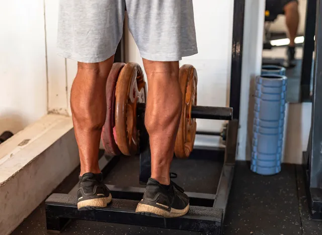 Dedicated anonymous man at the gym setting does calf raises on a weight-loaded machine with plates, focusing on lower body strength.